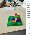 Small brick structure on a green baseplate displayed on a wooden table. The structure consists of various colored bricks, including red, pink, blue, yellow, and purple. Plastic cubes  131125604