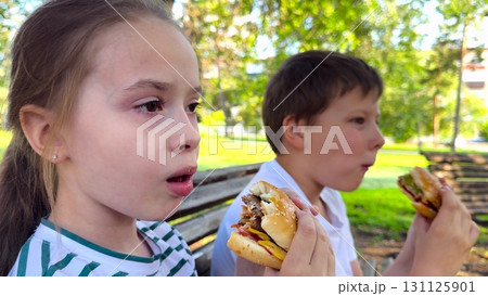 school children eat big hamburger, kids eat burger park, group children friends eat cutlet bun, joyful summer picnic for teens, sitting on a bench under the trees, biting into juicy burgers, sunny school children eat big hamburger, kids eat burger park, group children friends eat cutlet bun, joyful summer picnic for teens, sitting on a bench under the trees, biting into juicy burgers, sunny 131125901