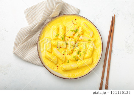 Traditional korean tteokbokki in creamy cheese sauce with garnish, wooden chopsticks on rustic white background top view 131126125