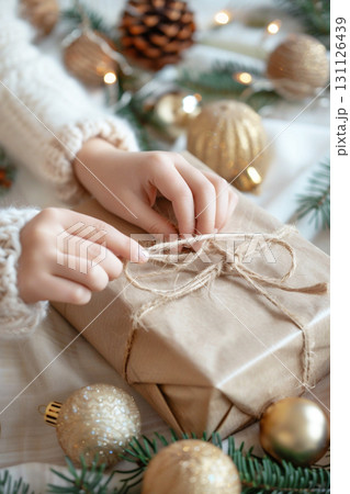 Hands wrapping eco-friendly Christmas gift with natural decor and festive ornaments 131126439