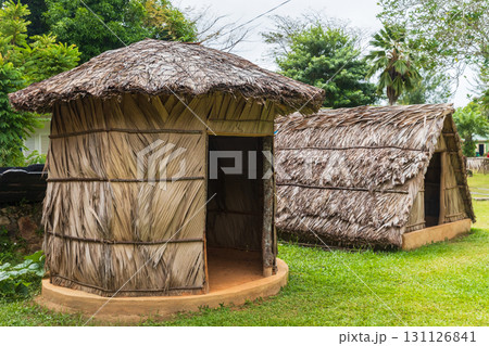 A pair of traditional thatched huts stand on grassy ground in a lush. Mahe, Seychelles 131126841