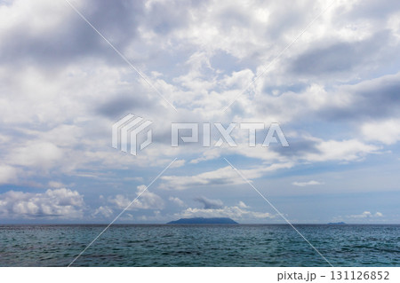 Serene seascape featuring calm waters, a distant island beneath a blue sky 131126852