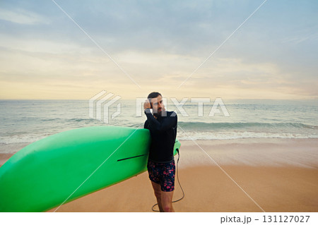 bearded man with surfboard standing near a beach. Man with surfing board outdoors on a summer day. 131127027