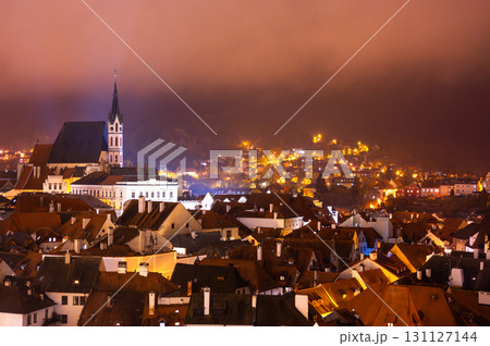 A panoramic night view of Cesky Krumlov, showcasing the rooftops, illuminated buildings, and the Church of St. Vitus beautifully lit up against the dark sky 131127144