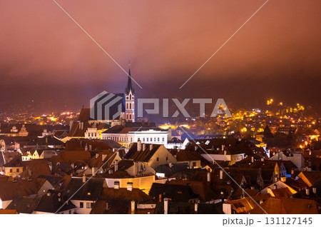 A panoramic night view of Cesky Krumlov, showcasing the rooftops, illuminated buildings, and the Church of St. Vitus beautifully lit up against the dark sky 131127145