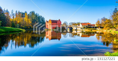 Panoramic view of Cervena Lhota Castle in the Czech Republic, surrounded by a lake reflecting its image. Autumn trees in vibrant colors and sunny weather create a picturesque, serene scene. Panoramic view of Cervena Lhota Castle in the Czech Republic, surrounded by a lake reflecting its image. Autumn trees in vibrant colors and sunny weather create a picturesque, serene scene. 131127221