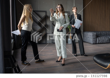Group of professional women in office during meeting, one pointing at window while colleagues listen, teamwork and planning concept. 131127398