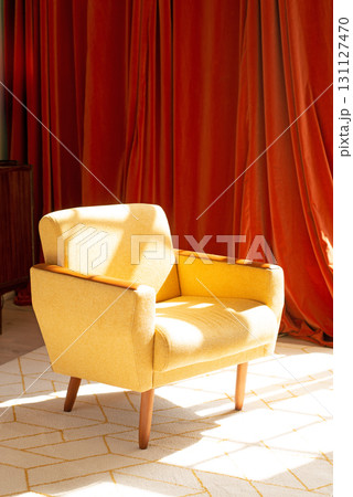 A modern yellow armchair in a stylish interior, with warm orange curtains and a sunbeam creating a cozy, elegant atmosphere. 131127470