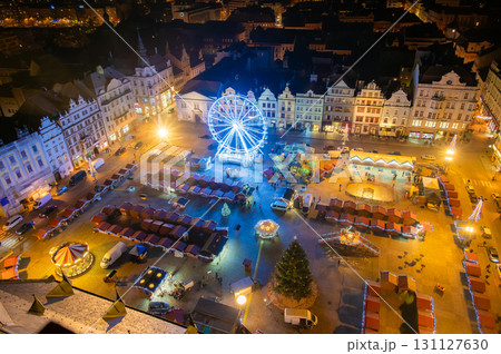 An aerial night shot of the Christmas markets in the square in Pilsen, featuring vibrant stalls surrounding the plaza and a large Ferris wheel lighting up the festive scene 131127630