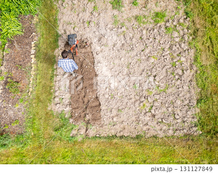 Young farmer man is cultivating the field with machine. Aerial drone top down view of small field in old fashioned garden. Concept of home agriculture. Young farmer man is cultivating the field with machine. Aerial drone top down view of small field in old fashioned garden. Concept of home agriculture. 131127849