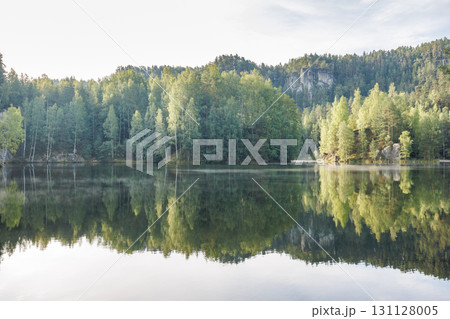 The Piskovna lake in Adrspach-Teplice Rocks area, in Hradec Kralove Region in the Czech Republic, Europe. Serene lake mirroring the lush forest and rock formations under a bright, clear sky. 131128005
