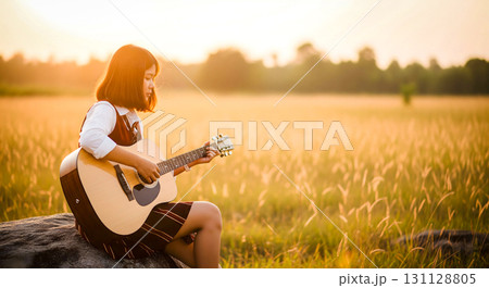 Woman Playing Acoustic Guitar in Field at Sunset 131128805