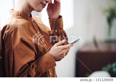 窓際でスマートフォンを操作する女性の手元 131129089