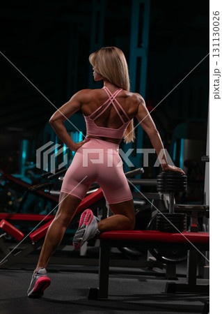blonde woman is exercising at the gym positioned near weights. She wears a pink outfit and appears strong as she focuses on her workout. The gym has a modern sleek design. blonde woman is exercising at the gym positioned near weights. She wears a pink outfit and appears strong as she focuses on her workout. The gym has a modern sleek design. 131130026