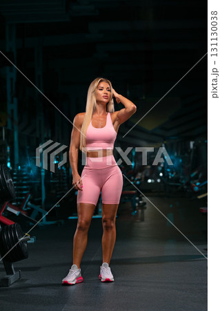 blonde woman stands confidently in a gym dressed in a pink workout outfit. She is taking a moment to adjust her hair after an intense training session. The atmosphere is energetic and motivating. blonde woman stands confidently in a gym dressed in a pink workout outfit. She is taking a moment to adjust her hair after an intense training session. The atmosphere is energetic and motivating. 131130038