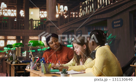 Black teacher mentoring her teen girls students with an assignment, teaching academic concepts and enhancing their knowledge through practical exercises. Private lessons at the library. Camera A. 131130640