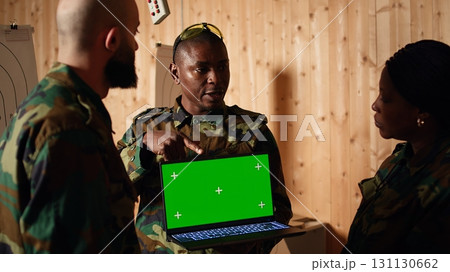 Team of military units at shooting range watching video on isolated screen laptop to learn necessary combat skills. Army soldiers looking at instructions on mockup notebook during training, camera A Team of military units at shooting range watching video on isolated screen laptop to learn necessary combat skills. Army soldiers looking at instructions on mockup notebook during training, camera A 131130662