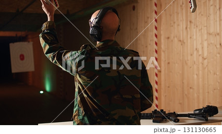 Army soldier in shooting range reloads pistol, shooting target, testing accuracy, looking at results. Military man in firing range practices with weapon, checking to see if he shot bullseye, camera A Army soldier in shooting range reloads pistol, shooting target, testing accuracy, looking at results. Military man in firing range practices with weapon, checking to see if he shot bullseye, camera A 131130665