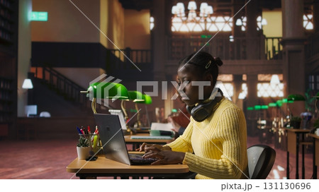 Teenager girl working on a foreign language assignment in the school library, consulting books and dictionaries to finish the homework project. Productive study habits and research at desk. Camera A. 131130696