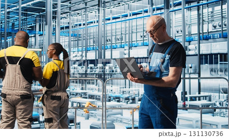 Industry 4.0 industrial plant senior engineer automating robotic machines using laptop software. Experienced technician implementing AI features in smart factory using notebook, camera A Industry 4.0 industrial plant senior engineer automating robotic machines using laptop software. Experienced technician implementing AI features in smart factory using notebook, camera A 131130736