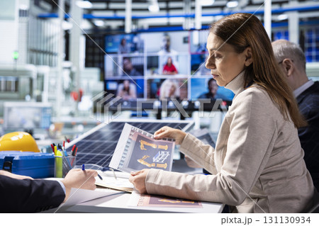 Factory admins look over schematics during video call, brainstorming improvements for operational efficiency. Shareholders look over production plant lines blueprints in videoconference 131130934
