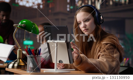 Young female adult listening to therapy music and working on her bachelor paper, using ambient sounds to help her focus in the university library. Student does academic research. Camera A. 131130950