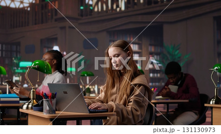 Student girl reading a literature book to collect citations for her diploma paper, ensuring a plagiarism free bachelor paperwork at the library. Pupil takes notes on her laptop. Camera A. 131130973