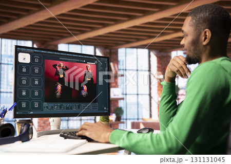 Smiling man in apartment workspace using AI software on computer display turning text prompt into photos. Upbeat african american person in home office uses text to image generative models on PC 131131045