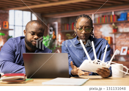 African american couple restarting their wireless router and checking network settings to resolve an internet error disrupting their freelance daily tasks. Signal loss during remote work. African american couple restarting their wireless router and checking network settings to resolve an internet error disrupting their freelance daily tasks. Signal loss during remote work. 131131048
