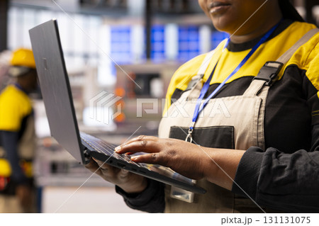 Closeup of technician ensuring smooth operation of automated production line, using software on laptop. African american industrial specialist optimizes manufacturing processes in smart factory. 131131075
