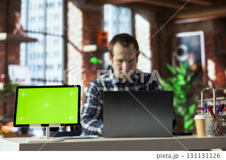 Teleworker in home office completing spreadsheets on laptop next to mockup tablet, entering data, calculating totals. Close up of green screen device next to bookkeeper using spreadsheet software Teleworker in home office completing spreadsheets on laptop next to mockup tablet, entering data, calculating totals. Close up of green screen device next to bookkeeper using spreadsheet software 131131126