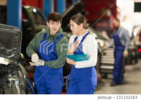 Car service manager discusses car repair problems with mechanic. He takes notes on paper Car service manager discusses car repair problems with mechanic. He takes notes on paper 131132163