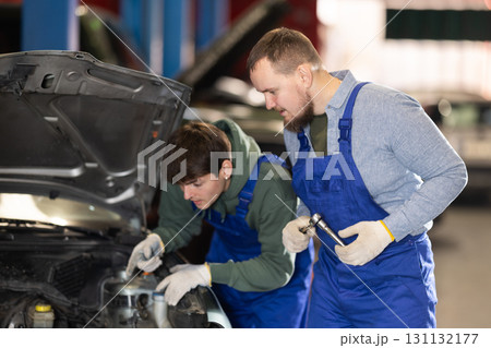 Two mechanics fixing a broken car in a service station Two mechanics fixing a broken car in a service station 131132177