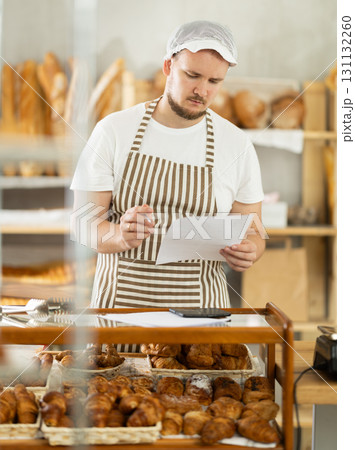 Bakery employee in apron examines documents, ponders debt restructuring Bakery employee in apron examines documents, ponders debt restructuring 131132260