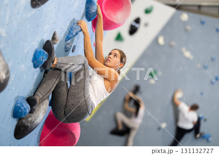 Sportive woman climbing on artificial rock wall in rock climbing gym Sportive woman climbing on artificial rock wall in rock climbing gym 131132727