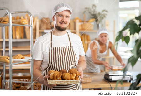 Male seller holds basket with finished products, shows many croissants Male seller holds basket with finished products, shows many croissants 131132827