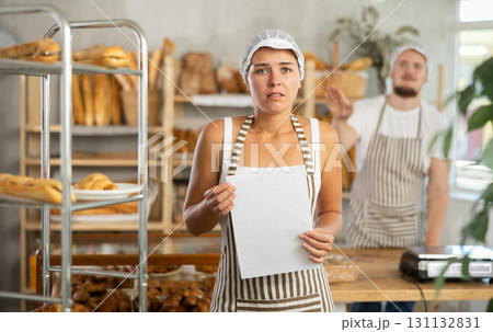 In bakery, confused female employee with documents during quarrel with guy boss 131132831