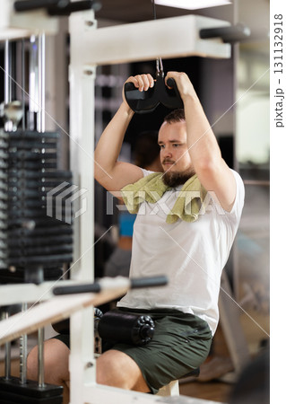 Man in gym performs exercises for arm muscles using cable crossover machine and pull weighted rope 131132918