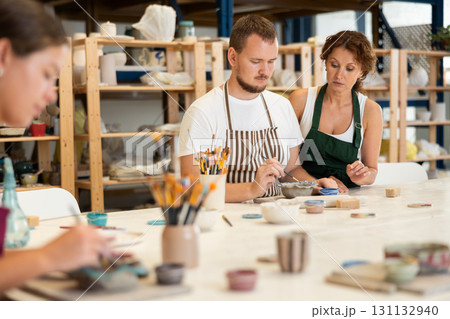 During master class, student paints clay vessel under guidance of female teacher. 131132940