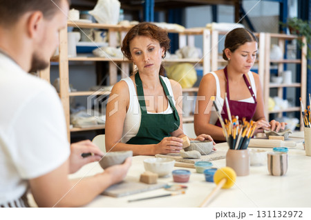 Three pottery workshop workers sculpt from raw clay 131132972