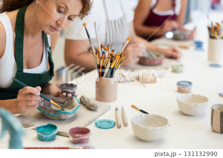 Close up girl paints bowl of clay during master class, top view. Close up girl paints bowl of clay during master class, top view. 131132990