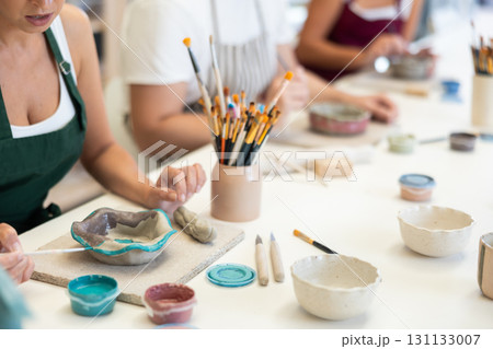 Close up girl paints bowl of clay during master class, top view. Close up girl paints bowl of clay during master class, top view. 131133007