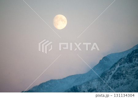 Near full moon slipping behind a mountain 131134304