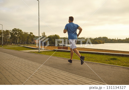 Sports guy runs through the city near the lake, back view Sports guy runs through the city near the lake, back view 131134327