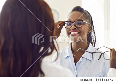 Optician gives new eyeglasses to a happy, smiling African American woman customer Optician gives new eyeglasses to a happy, smiling African American woman customer 131134373