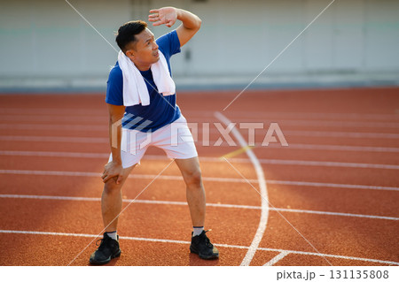Asian man in blue t shirt standing with hands on his knee and looking up with hand on his eyes. Asian man in blue t shirt standing with hands on his knee and looking up with hand on his eyes. 131135808