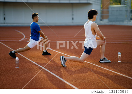 Two asian athlete men are stretching their legs muscles together on the racetrack in sports stadium. Two asian athlete men are stretching their legs muscles together on the racetrack in sports stadium. 131135955