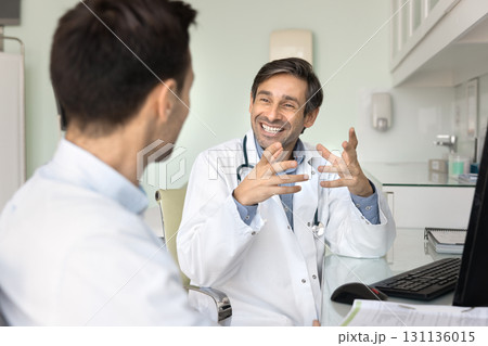 Smiling mature male doctor consulting male visitor after medical checkup Smiling mature male doctor consulting male visitor after medical checkup 131136015