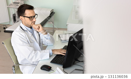 Thoughtful male doctor sit at workplace look at pc screen 131136036