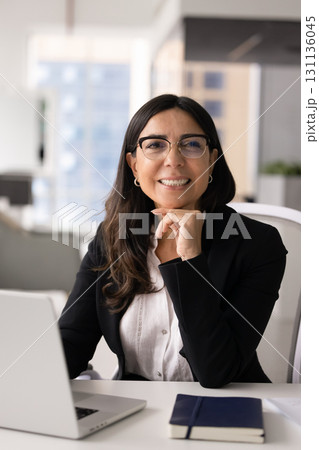 Positive mature business woman wearing elegant eyeglasses, posing at workplace Positive mature business woman wearing elegant eyeglasses, posing at workplace 131136045